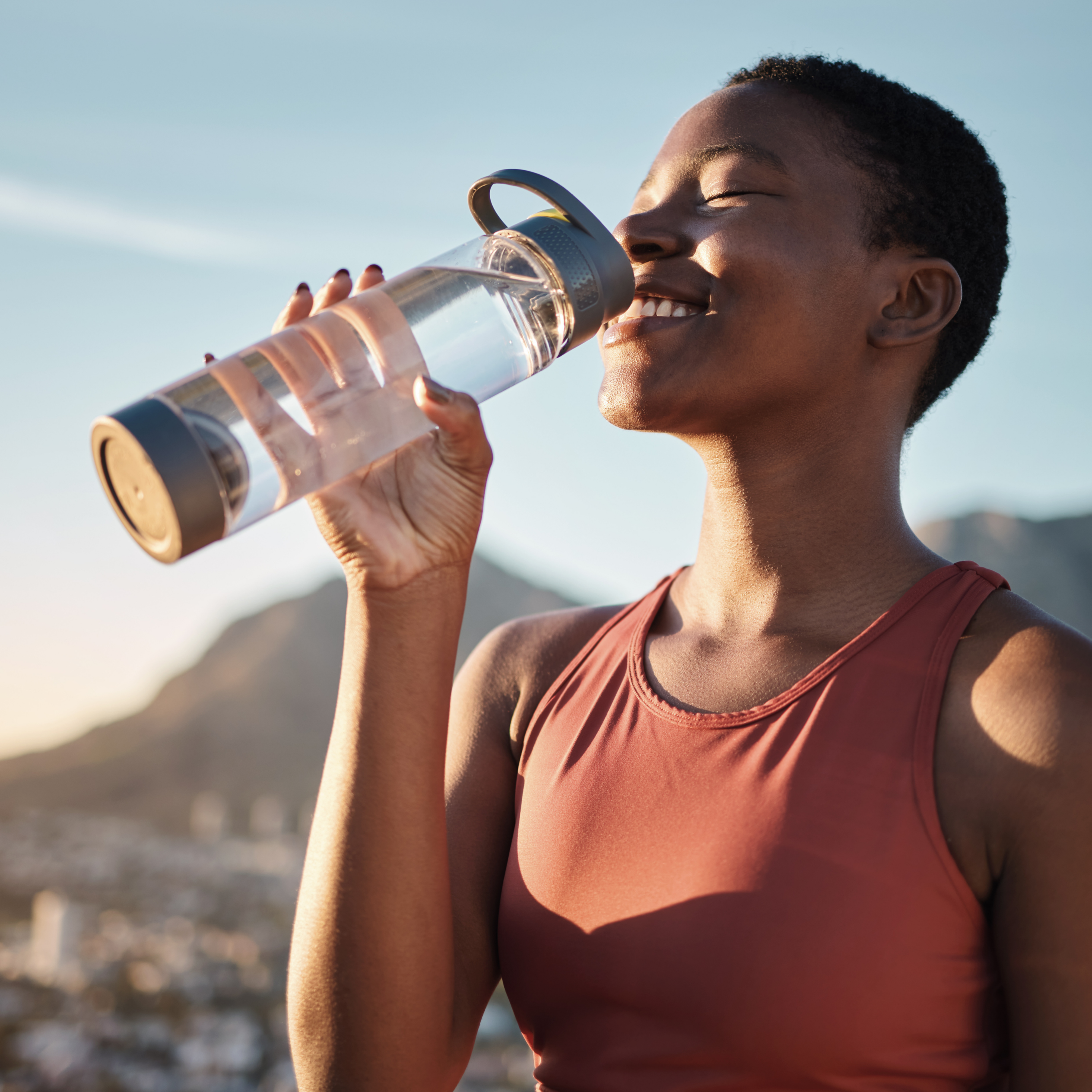 Woman drinking from a clear water bottle with a scenic background